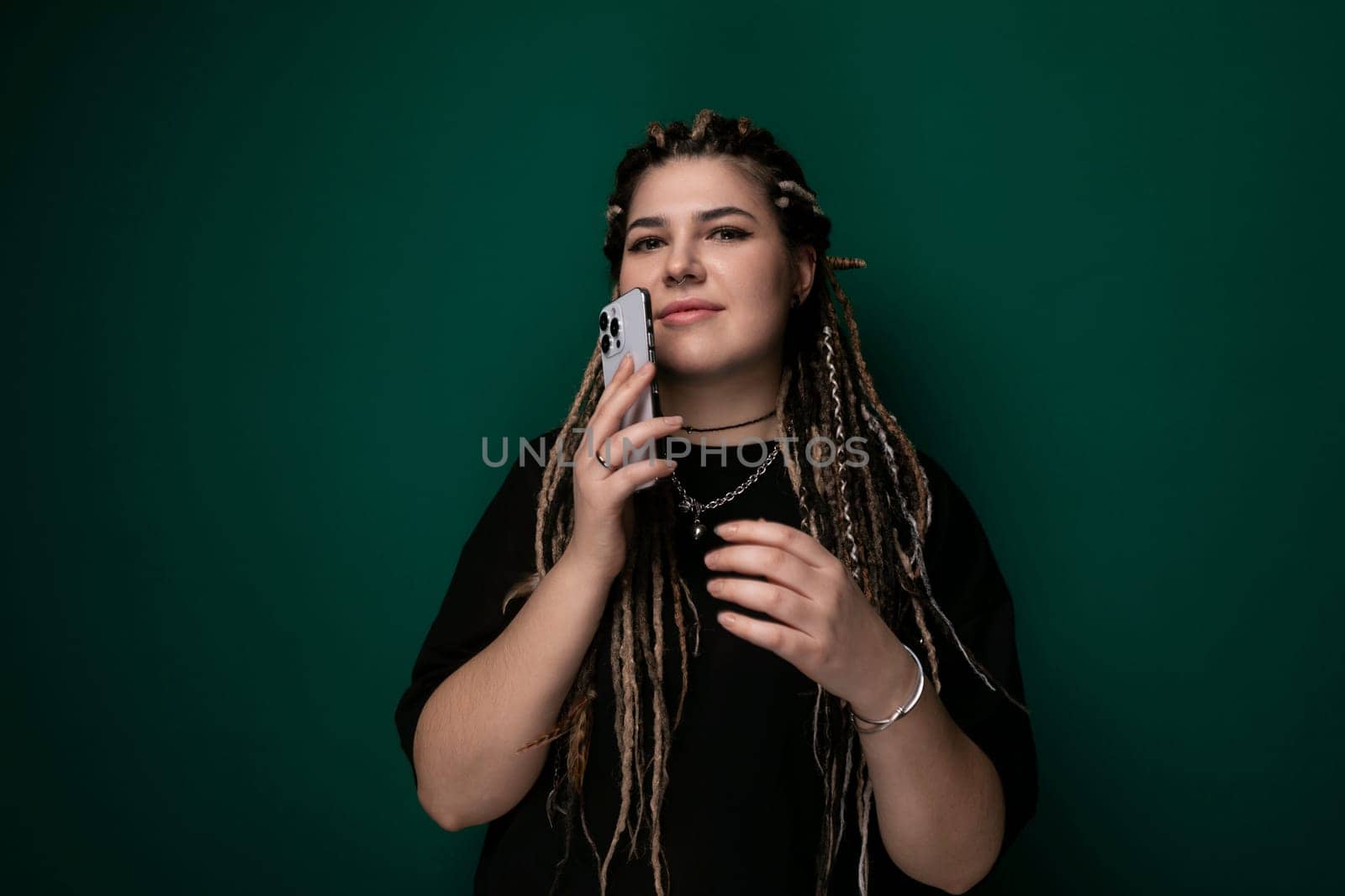 A woman with dreadlocks is holding a cell phone in her hand, looking at the screen while standing outdoors.