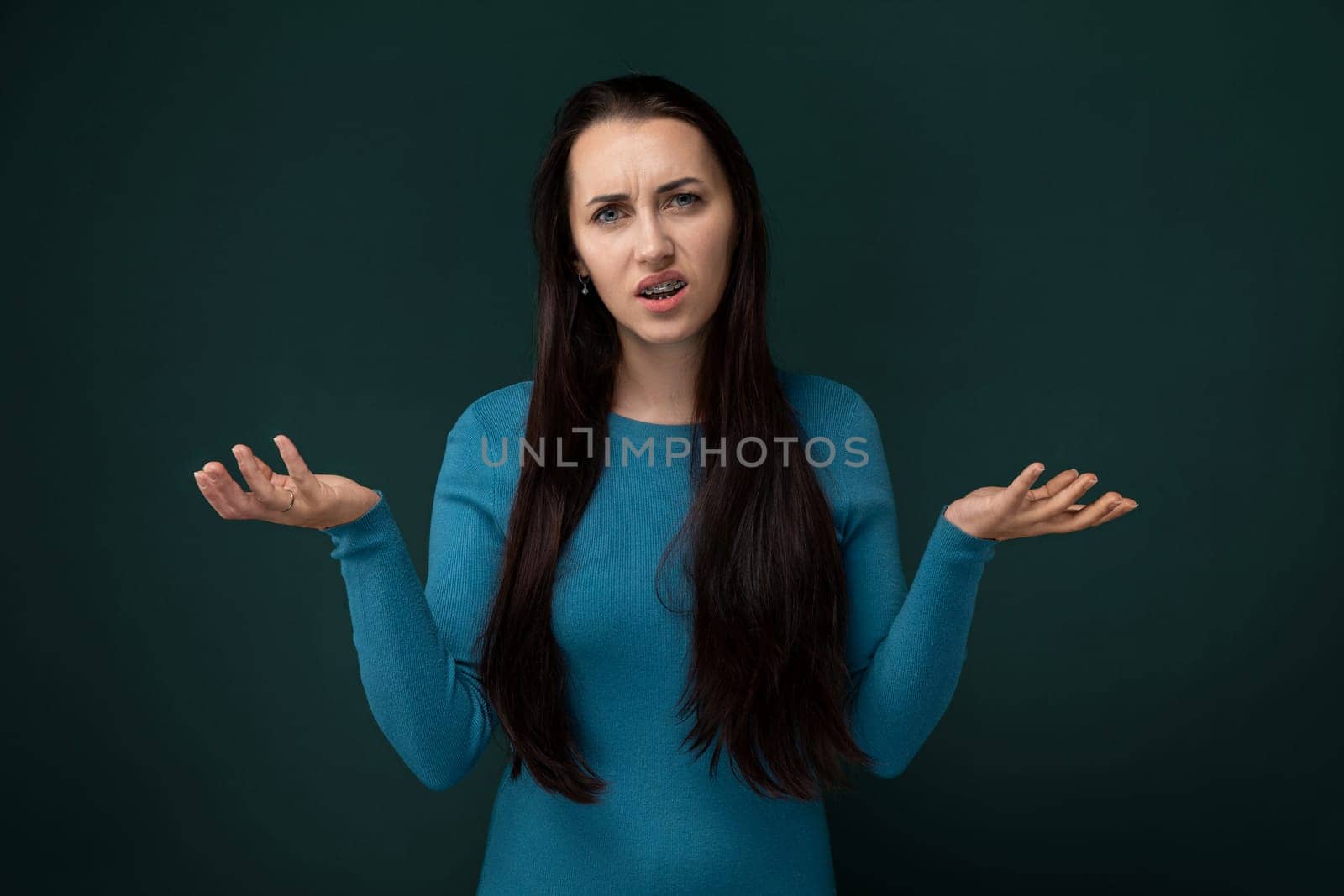 A woman wearing a blue dress is standing with her hands extended outward. She appears to be holding something or expressing a gesture of openness or invitation.