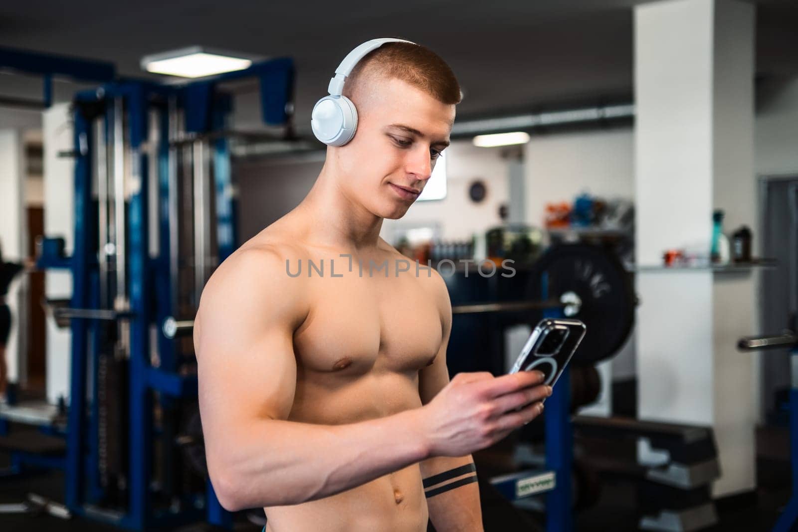 A shirtless man checks his phone during a workout in a gym