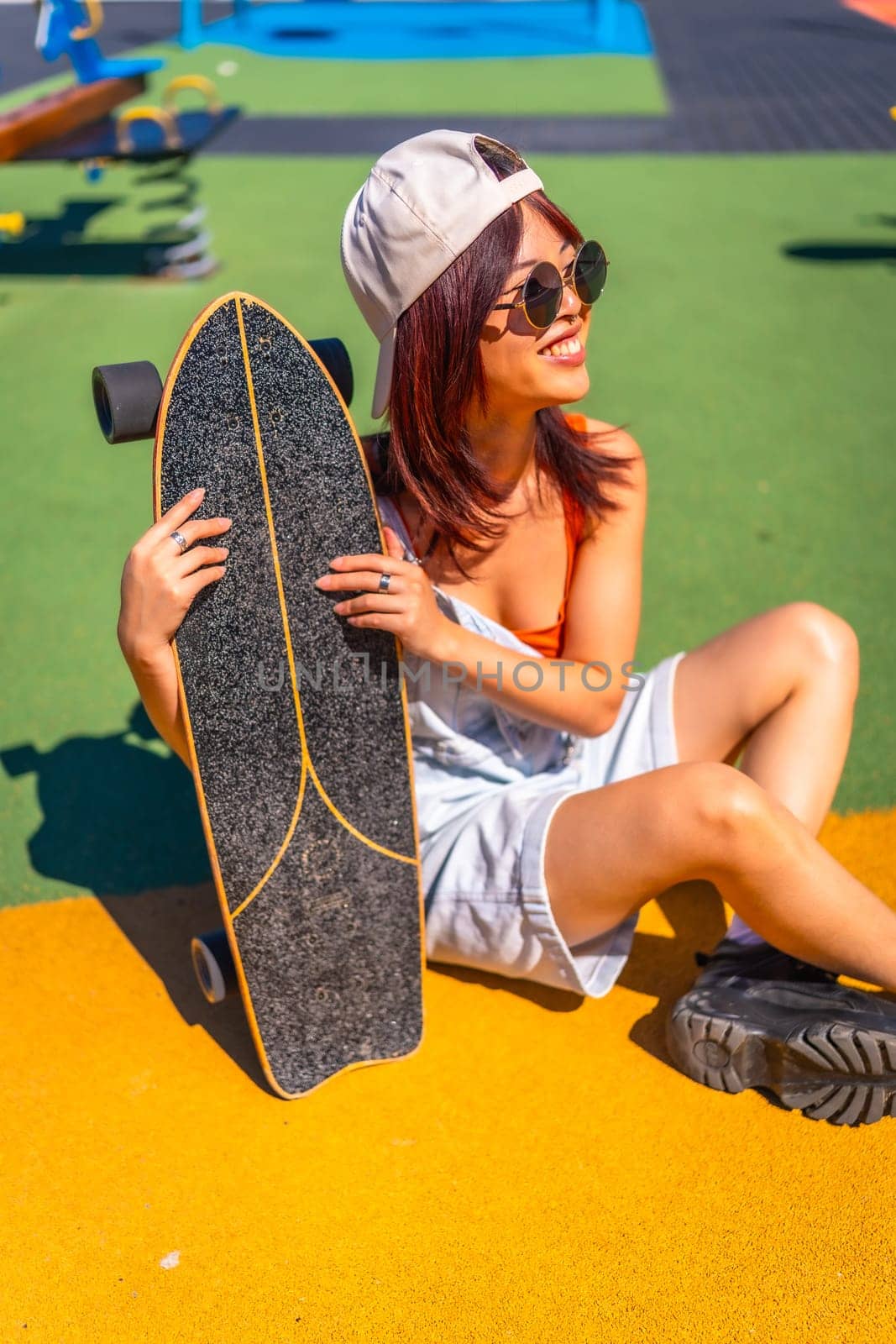 Vertical Portrait of a modern young woman with skateboard in a park with colorful ground