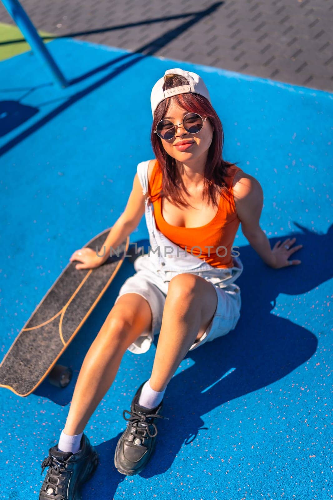 Vertical top view of a chinese young urban woman sitting on colorful skateboard park in the city