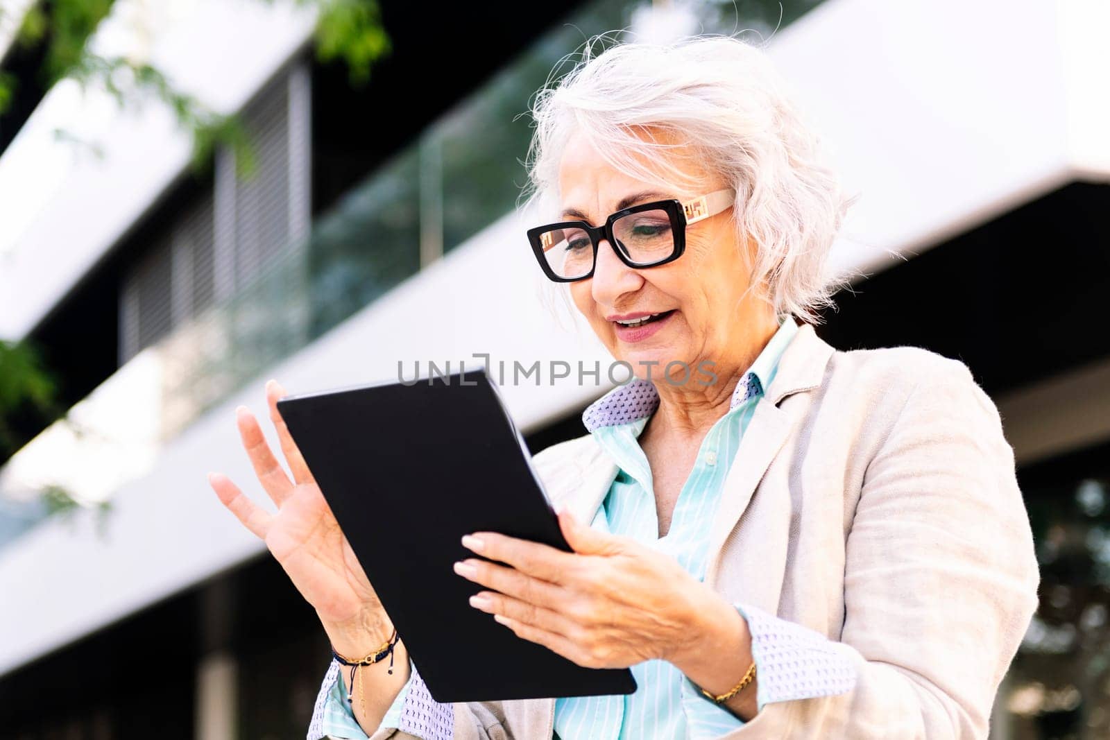 mature woman smiling happy while using digital tablet outdoors in the city, concept of urban lifestyle in adulthood and technology o communication