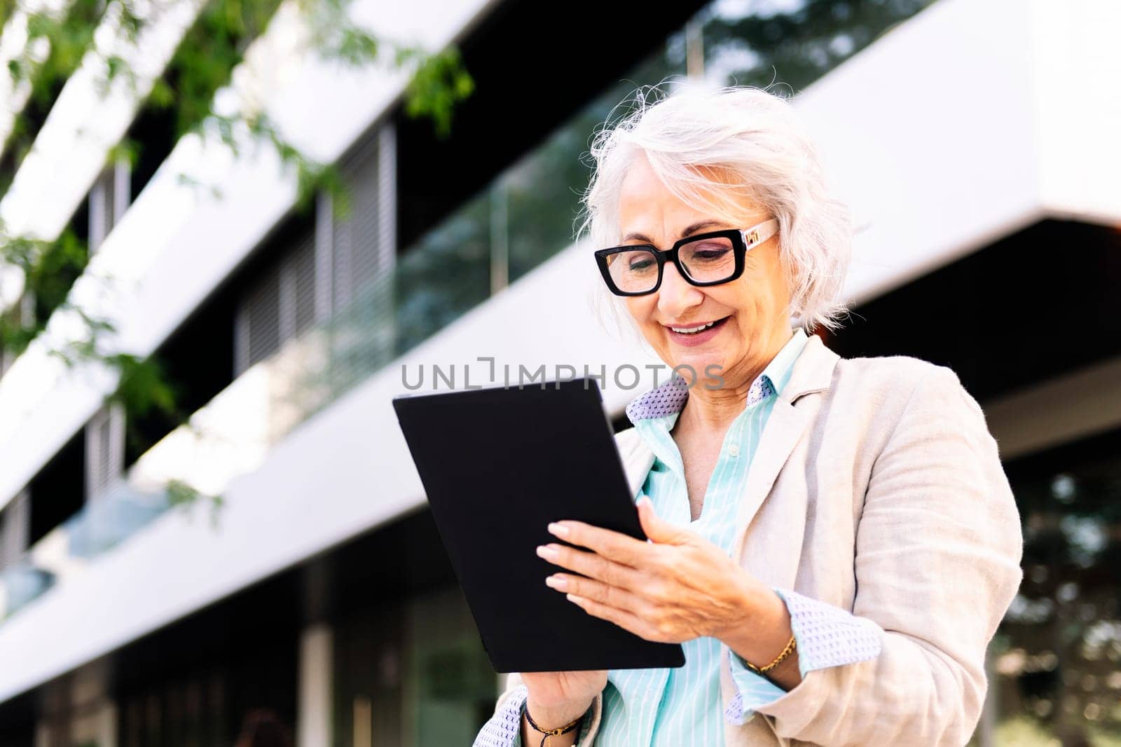 mature woman smiling happy while using digital tablet outdoors in the city, concept of urban lifestyle in adulthood and technology o communication, copyspace for text
