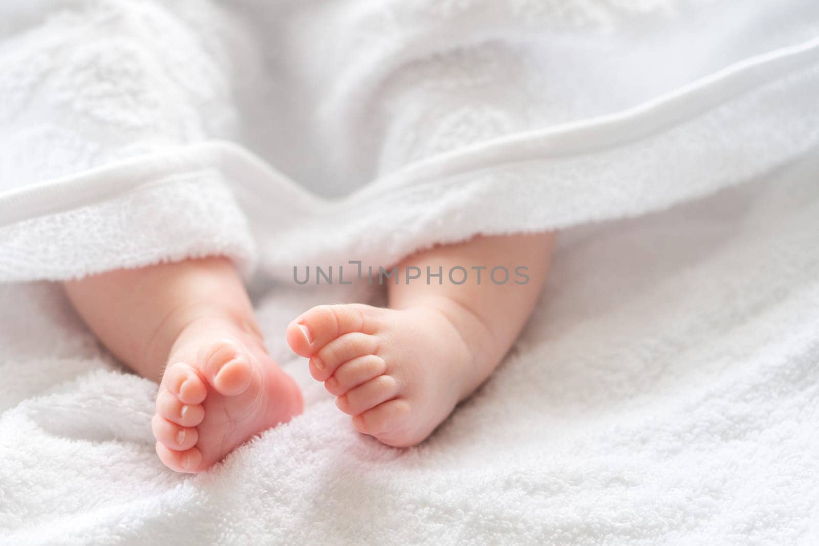 Soft white towel revealing the tiny feet and legs of an infant child, capturing the essence of post-bath calm and cleanliness