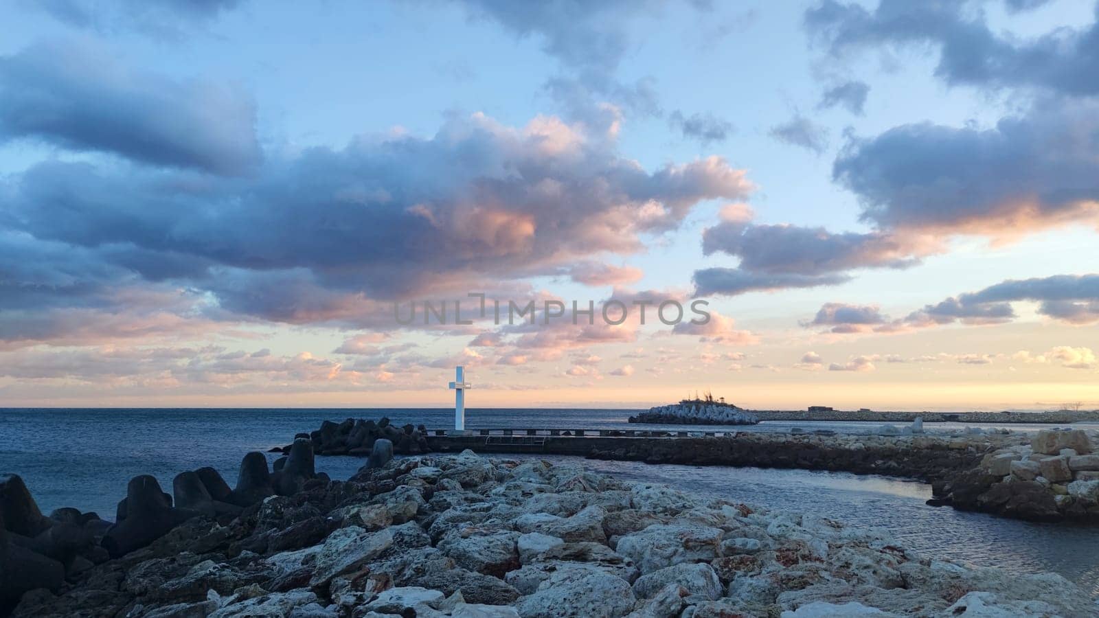 A large white cross on the pier of the Bulgarian resort of St. Konstantin and Elena against the backdrop of a cloudy sunset sky.