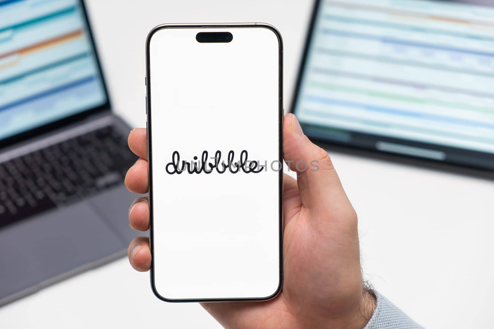 PRAGUE, CZECH REPUBLIC - JANUARY 21 2024: Dribbble logo on the screen of smartphone in mans hand on the workplace background.