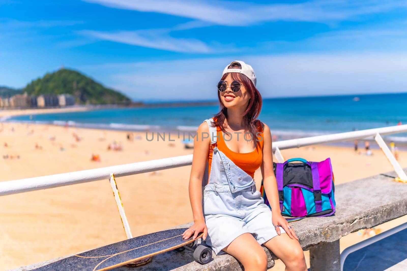 Horizontal photo with copy space of an asian young woman sitting on a promenade with skateboard in summer