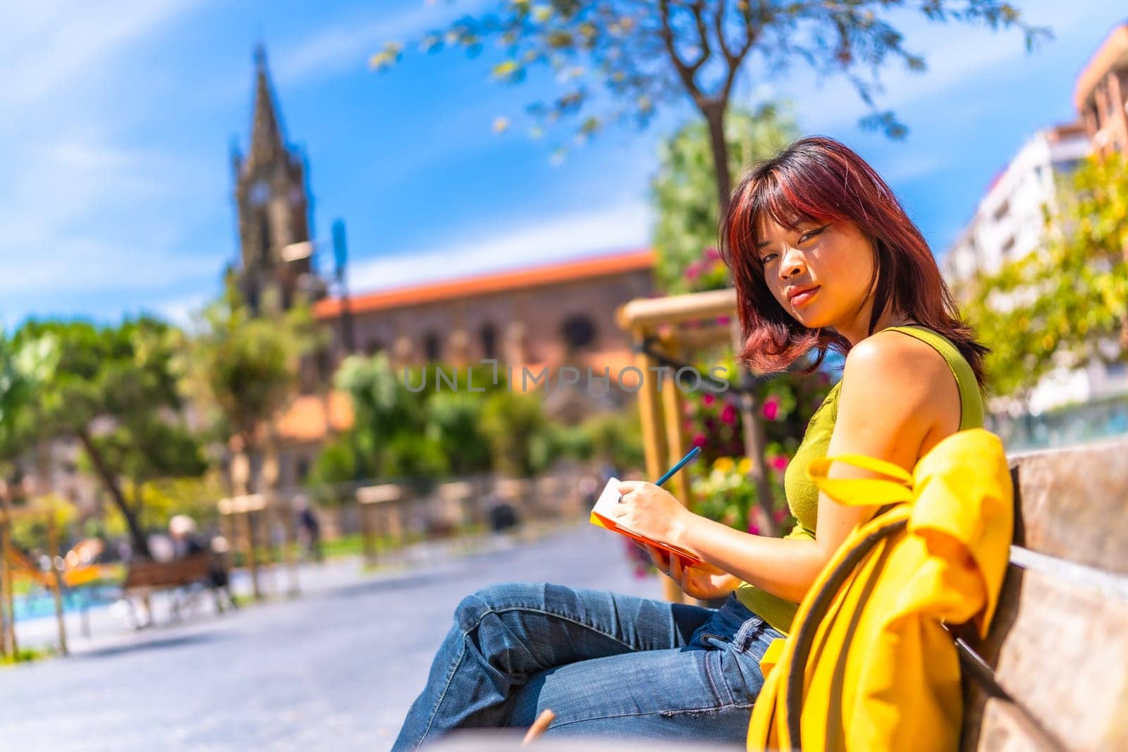 Asian cool young woman sketching sitting on a bench in the city in a sunny day