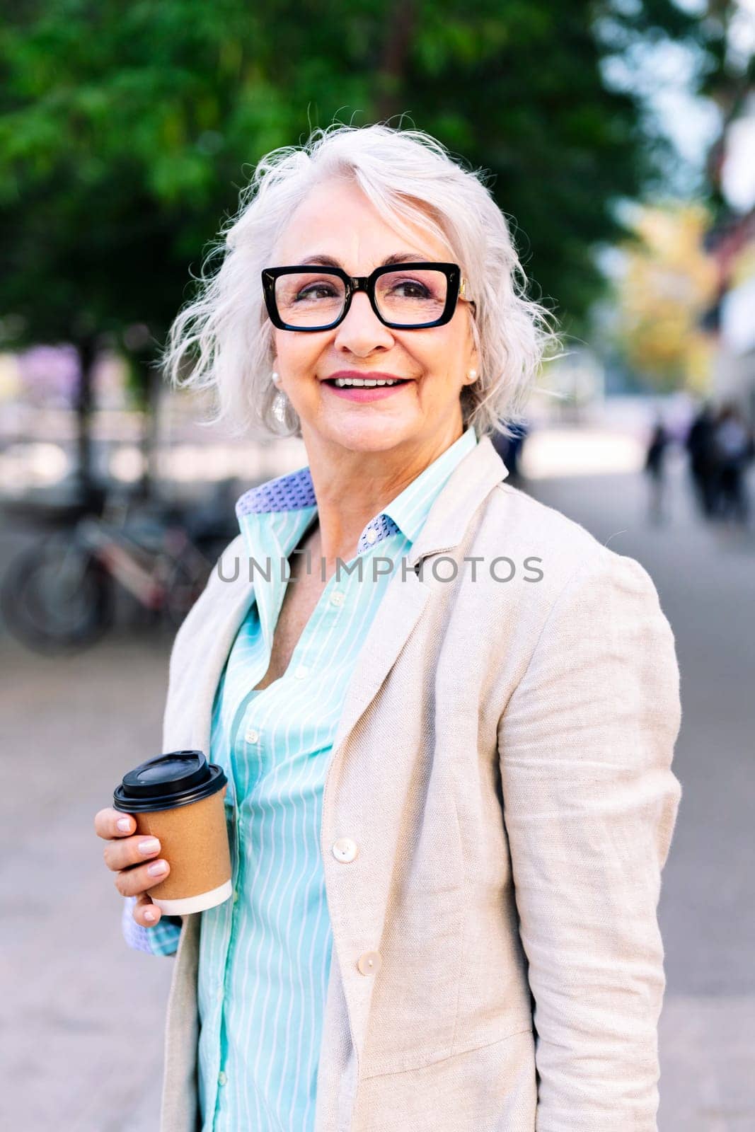 stylish mature woman walking happy through the city with a takeaway coffee in her hand, concept of active and urban lifestyle in adulthood