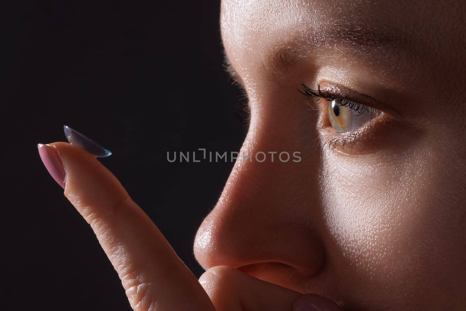 woman puts on contact lenses for vision close-up on a dark background, macro photo of contact lenses, astigmatic eyes, colored lenses