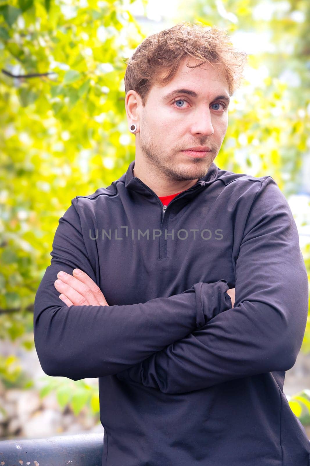Young Caucasian sportsman with defiant look and crossed arms looks at the camera