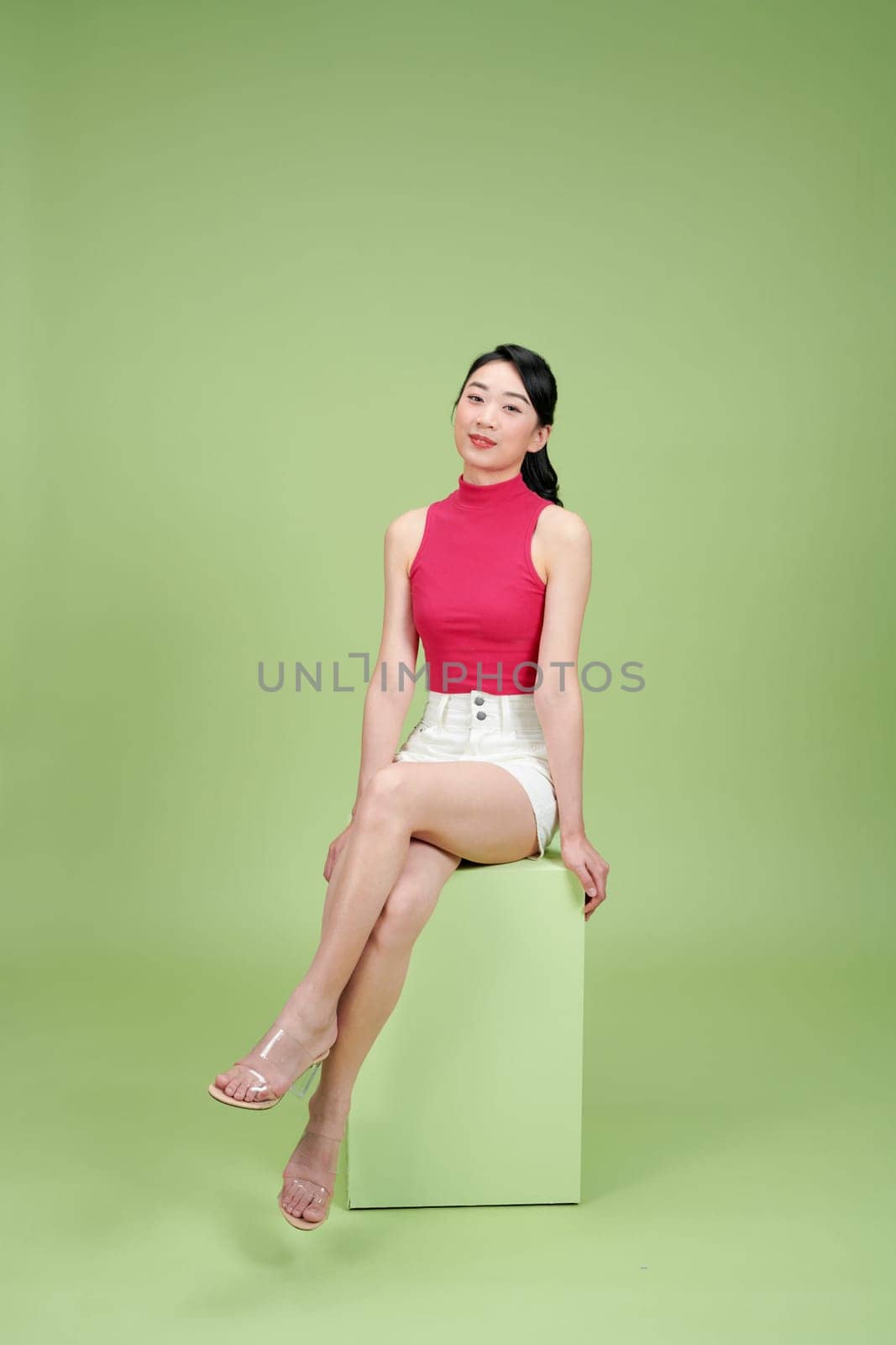 Young woman sitting on a green box against a green background, exuding confidence and style.
