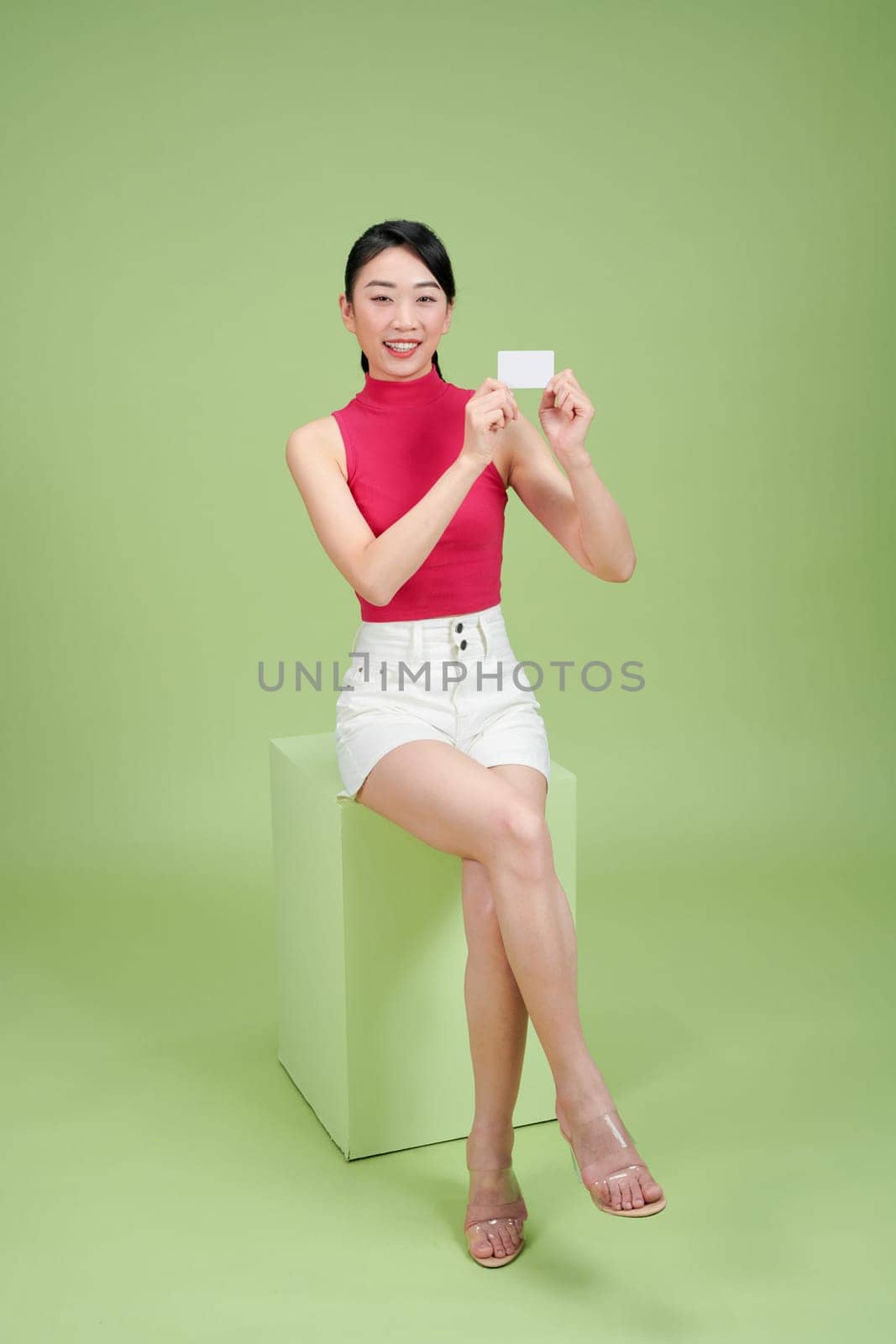 Cheerful woman holding at a blank card, standing against a green background