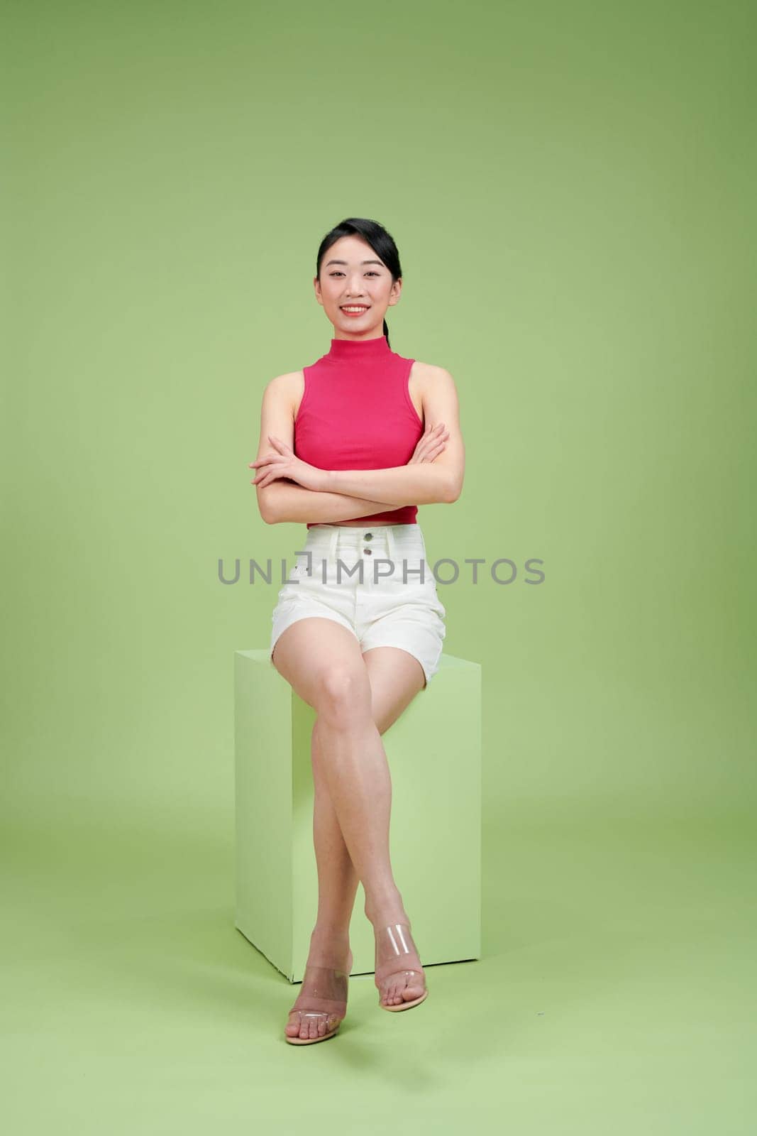 Confident woman sitting with crossed arms on a cube against a green background