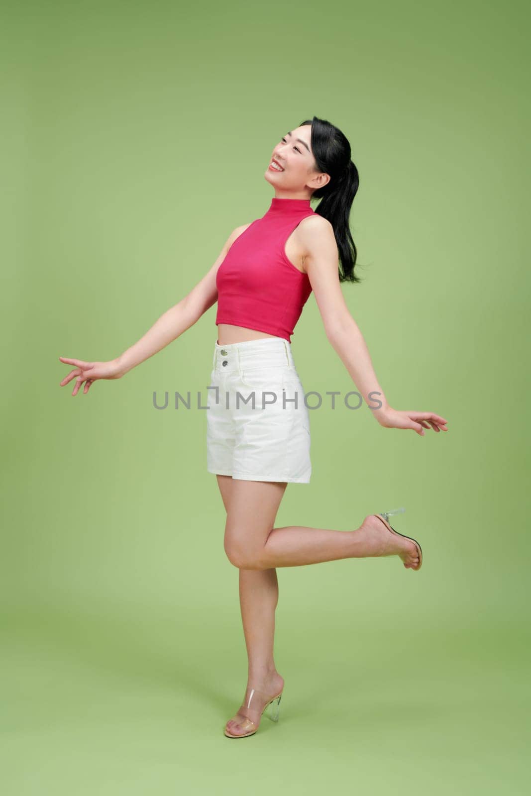 Cheerful woman posing playfully against a bright green background. She appears joyful and carefree.