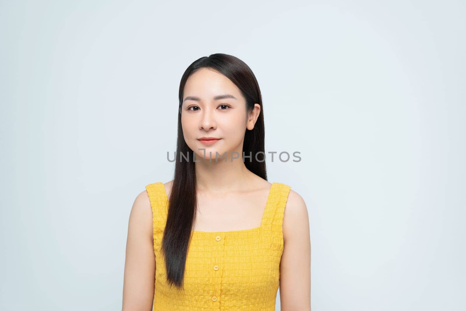Happy woman wearing a yellow top and blue jeans, smiling and posing against a white background. 