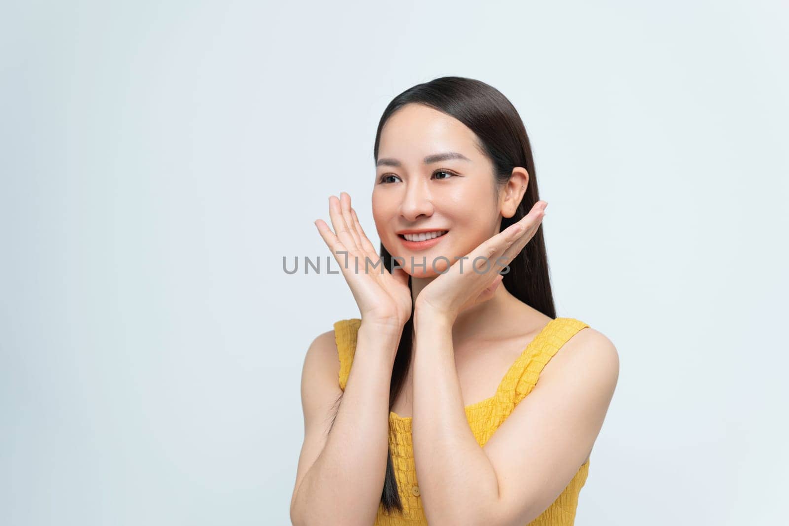A cheerful young woman smiles while posing with her hands on her face, exuding happiness and joy.