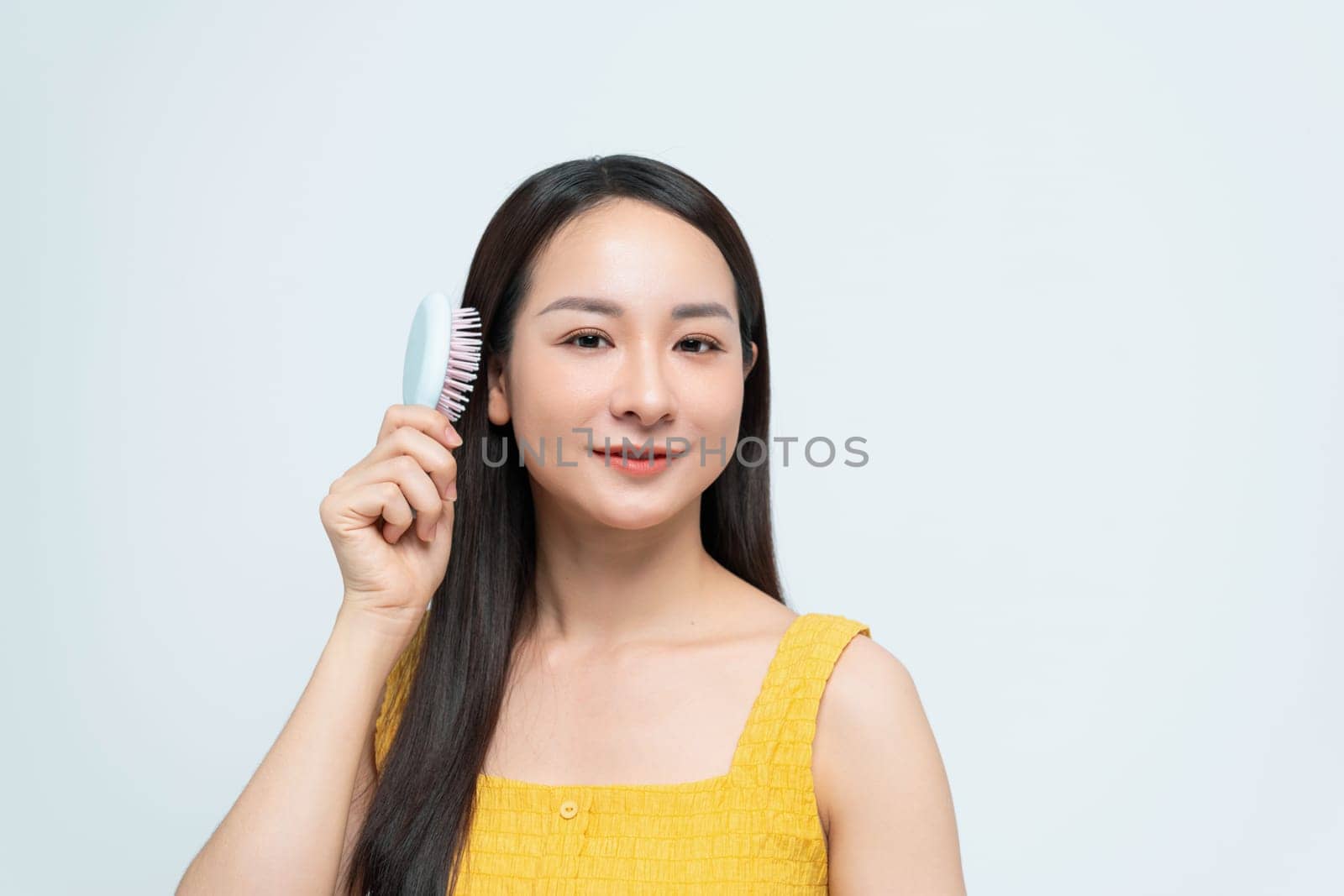 A young woman smiles confidently while holding a hairbrush against a light background, 