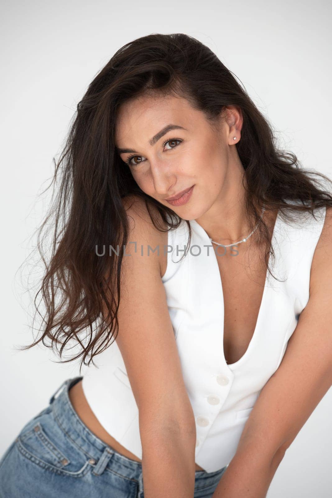 Happy beautiful girl posing in a new hot summer look. Wearing blue jeans and white waistcoat.