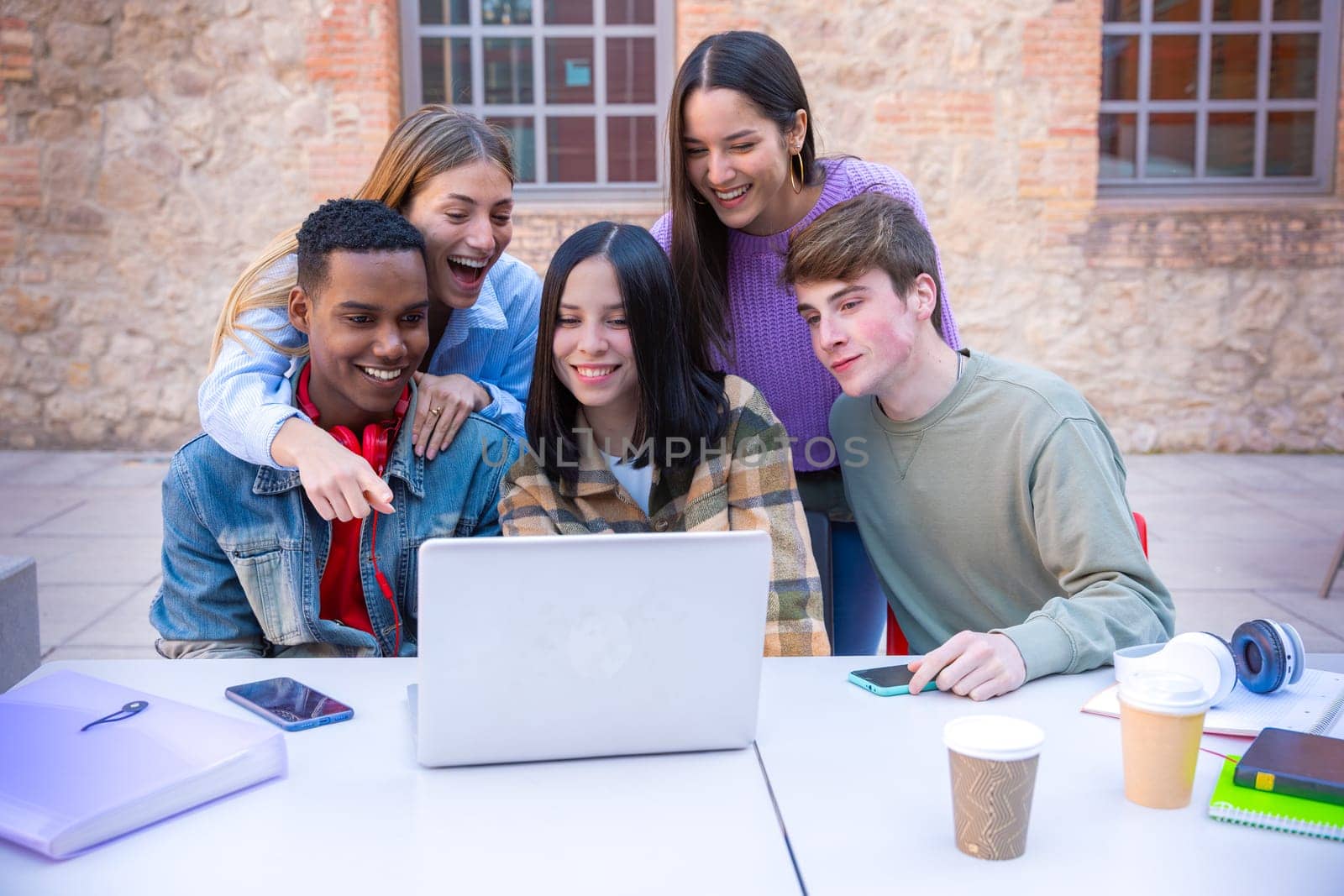 Five students with laptops and notes sit near the campus to review the exam.tudents with laptops sit near the campus and communicate. High quality photo