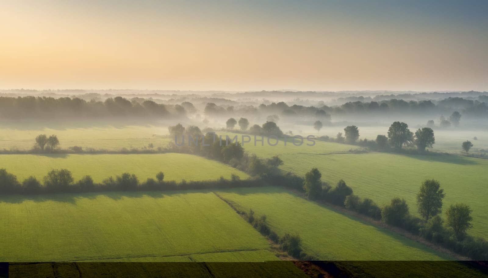 A misty sunrise paints the landscape in soft, ethereal hues. Layers of fog drape over rolling hills, while green fields stretch out in the foreground. The sun casts a warm glow, transforming the scenery into a dreamlike vista.