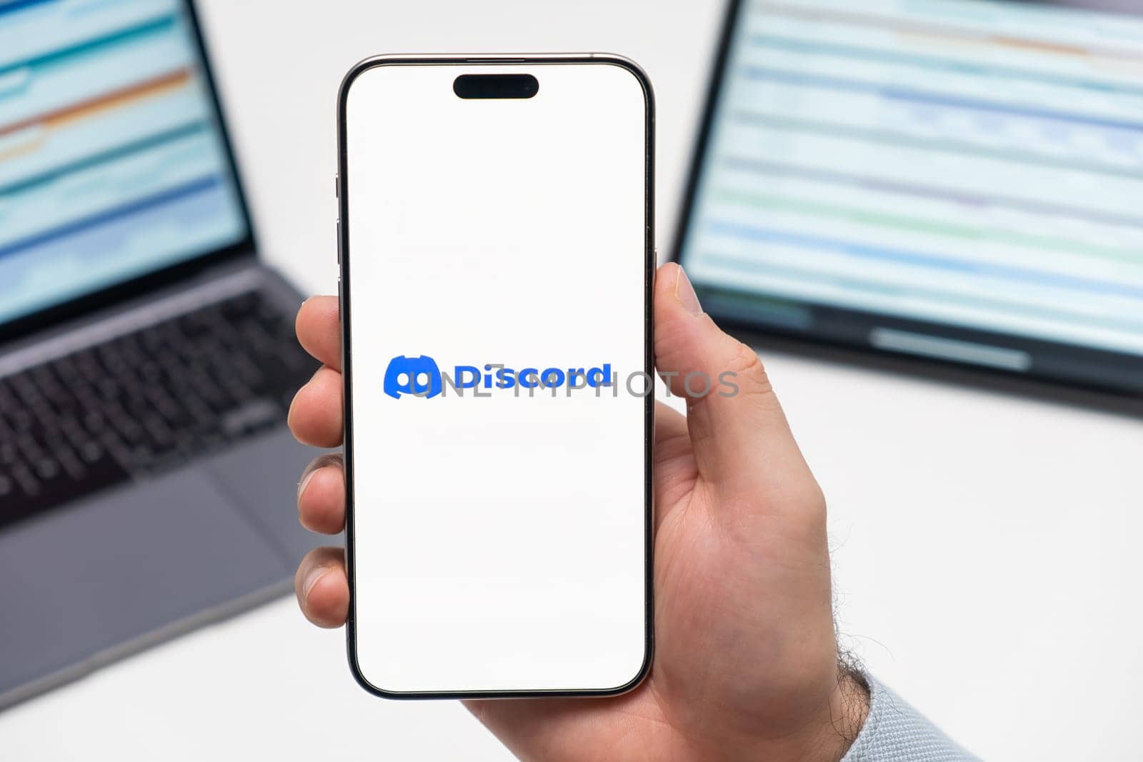 PRAGUE, CZECH REPUBLIC - JANUARY 21 2024: Discord logo on the screen of smartphone in mans hand on the workplace background.