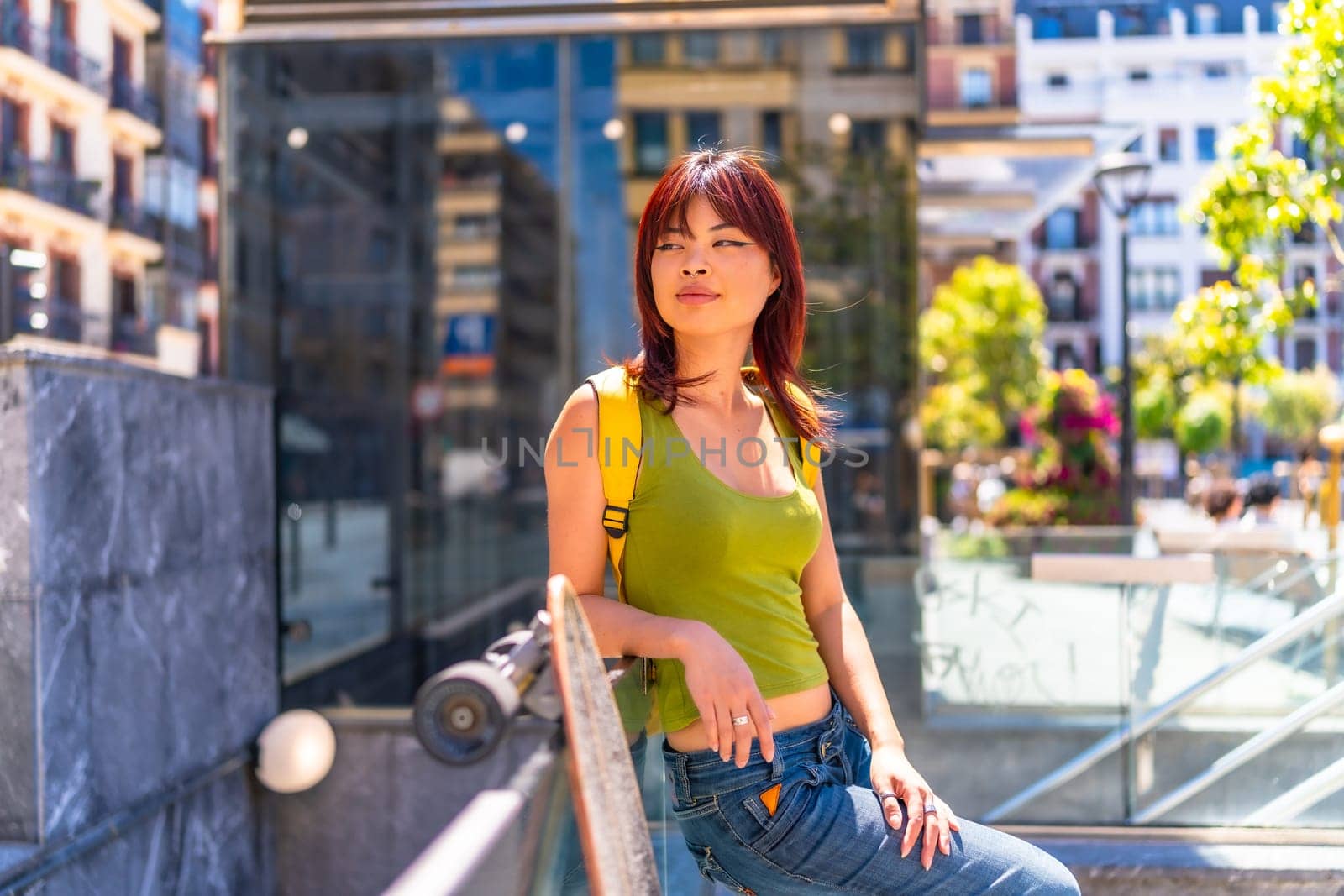 Portrait of a cool asian female young skater leaning on rail in the city