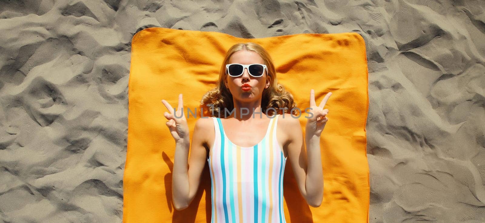 Summer vacation, tourism, happy cheerful young woman lying on sand on the beach, funny relaxed tourist girl lying on towel in swimsuit, glasses, top view