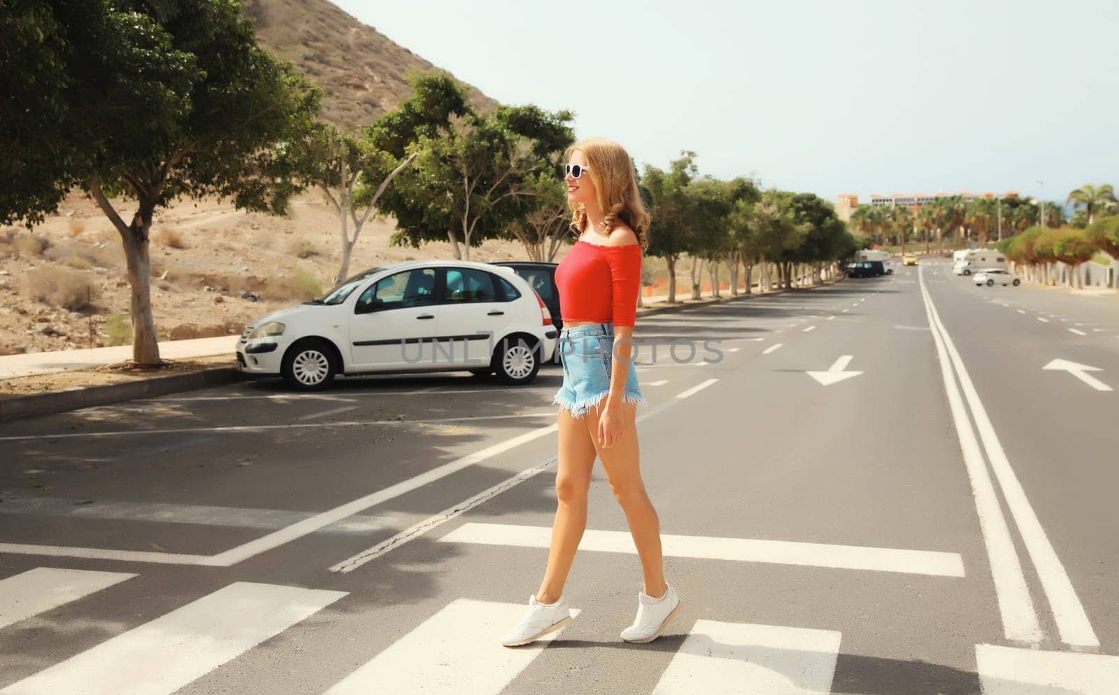 Happy beautiful caucasian young woman standing full-length on the road on a summer day