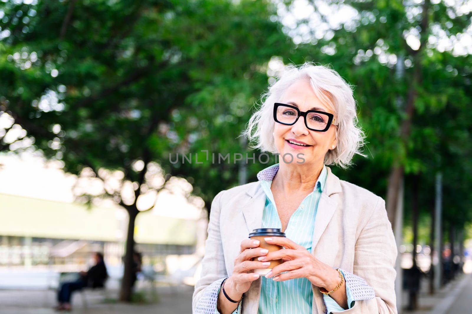 portrait of a stylish mature woman smiling happy looking at camera with a takeaway coffee in her hand, concept of active and urban lifestyle in adulthood