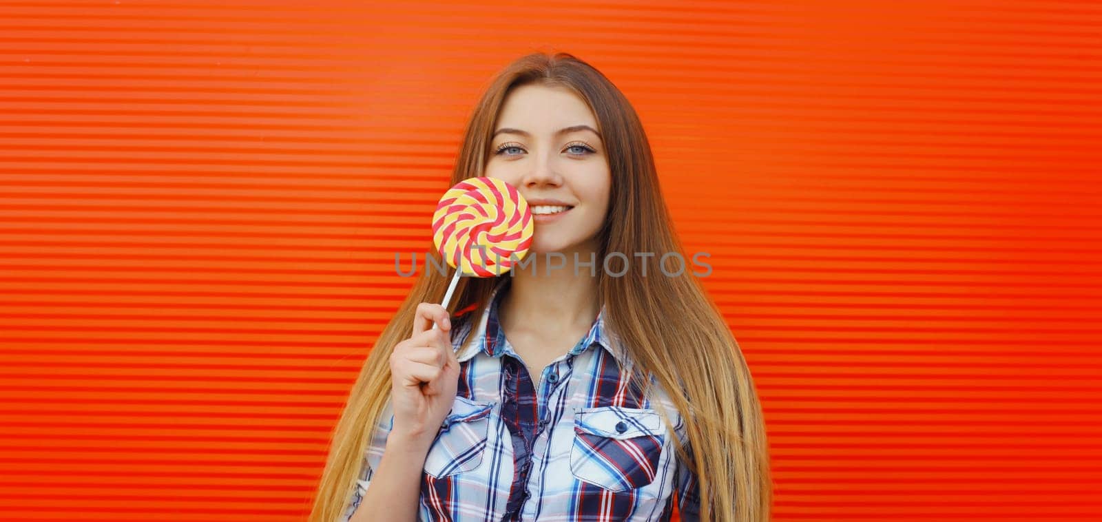 Portrait of happy cheerful smiling teenager girl holding colorful lollipop on red background
