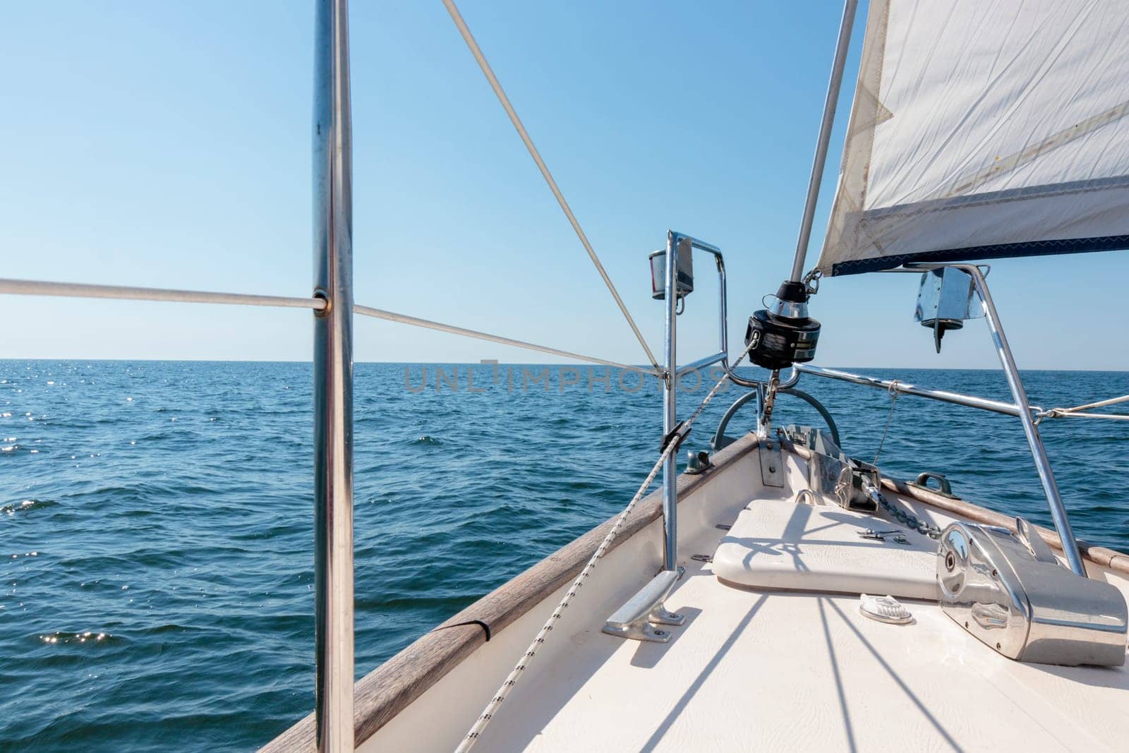 White yacht sailing on a sunny summer day. Top down view from the deck to the bow, mast and sails. Waves and water splashes. Clear blue sky. Gulf of Finland