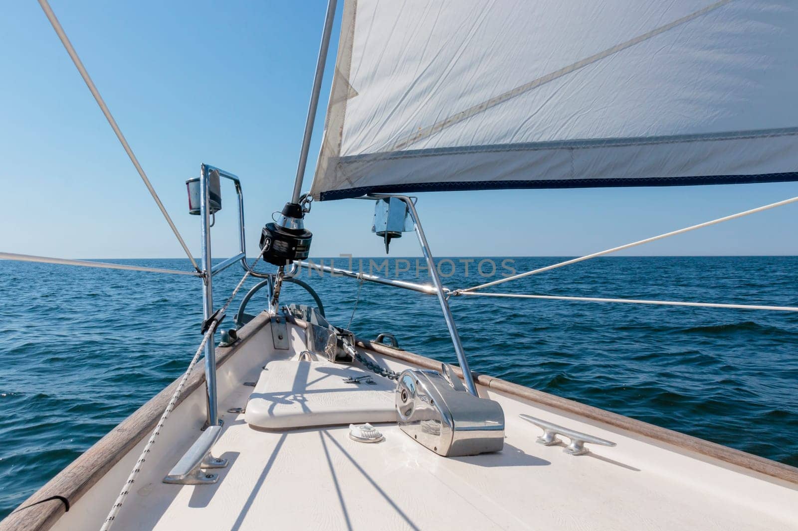 White yacht sailing on a sunny summer day. Top down view from the deck to the bow, mast and headsail. Waves and water splashes. Clear blue sky. Gulf of Finland