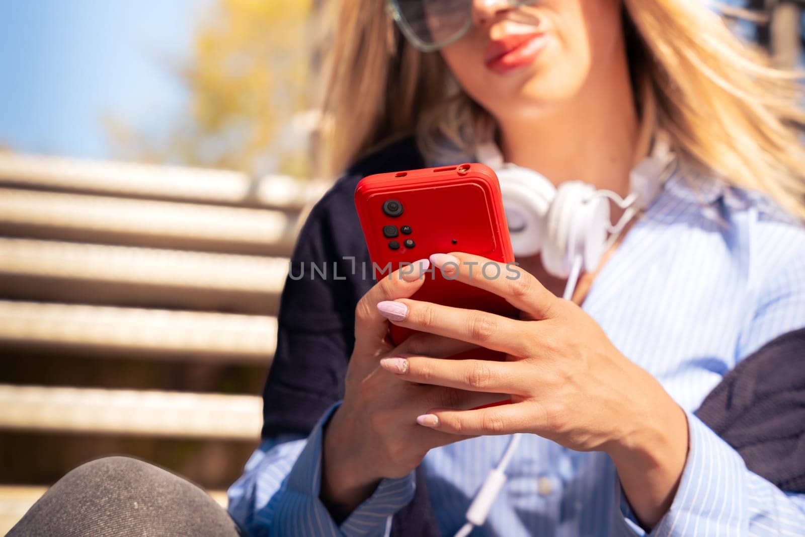 Portrait of a smiling young woman wearing headphones and sunglasses, using a social media app