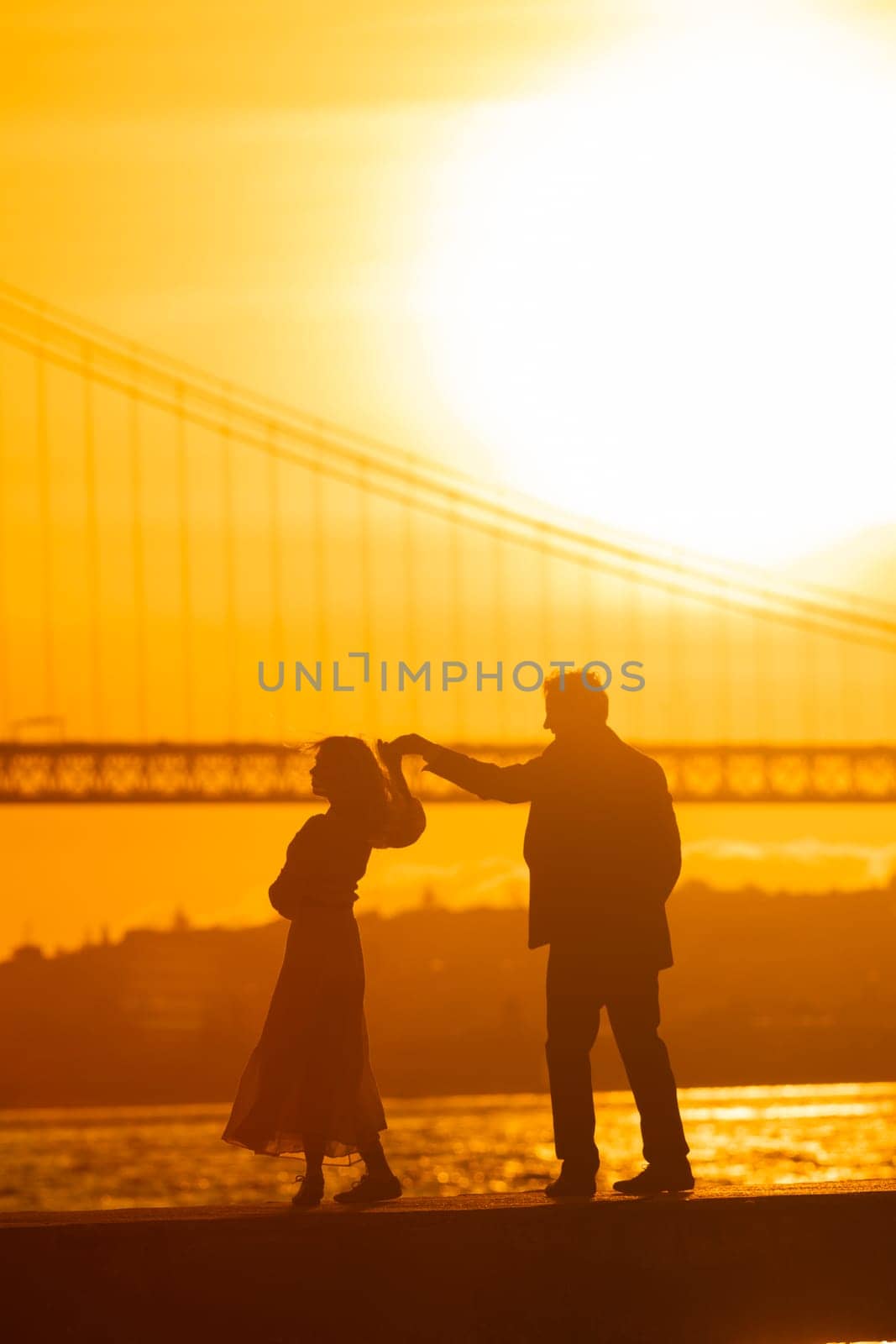 A silhouette of a man and woman dancing together at sunset. The bridge is visible in the background.