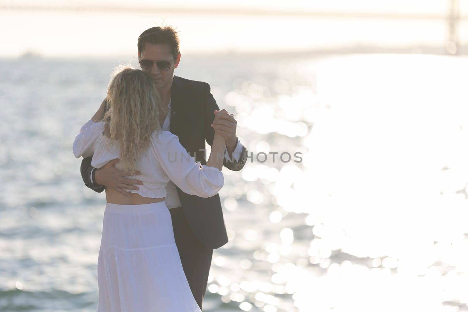 A man and woman dance together on a beach as the sun sets, creating a romantic and beautiful scene.