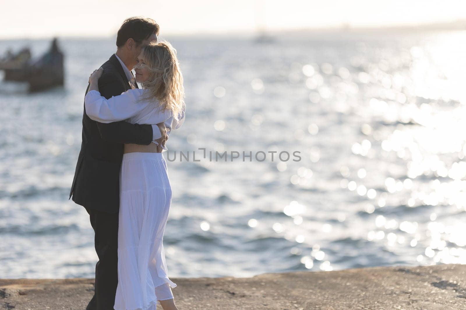 A man and woman dance on a rocky shoreline as the sun sets over the ocean.