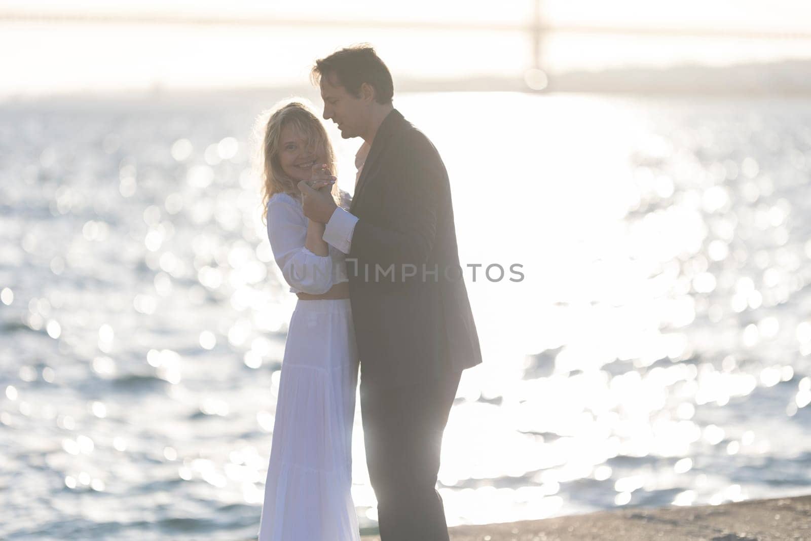 A man and woman dance together on a beach at sunset, with the water reflecting the golden light.