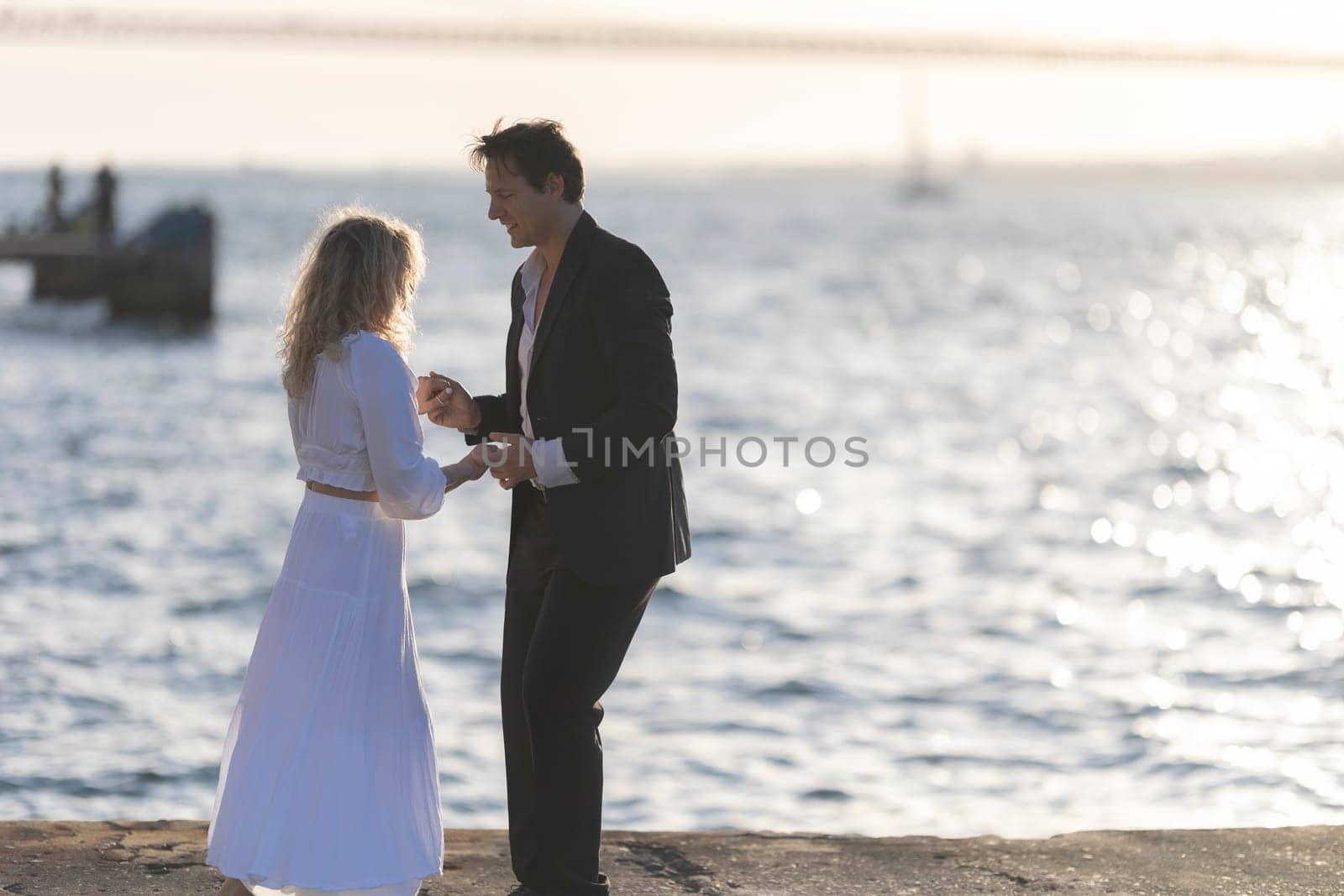 A man and woman dance together on a pier overlooking the ocean at sunset.