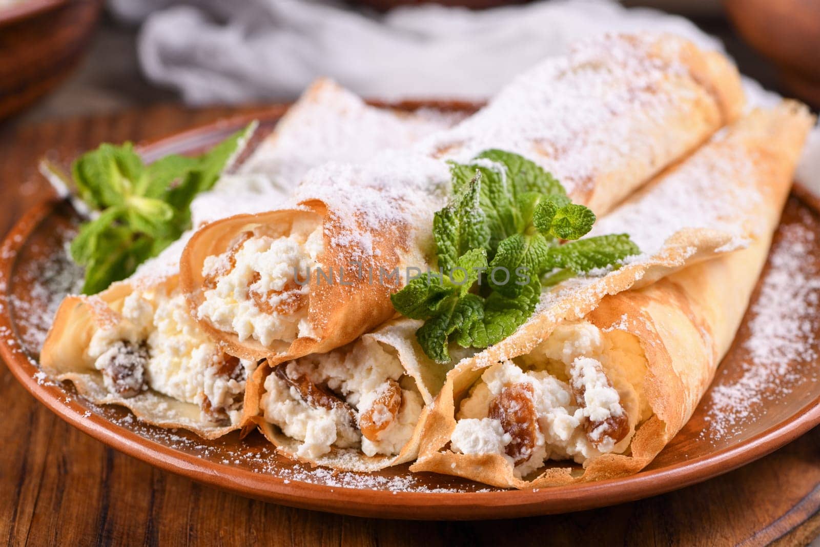 Thin pancakes filled with cottage cheese, honey and raisins, rolled in the form of a tube, sprinkled with powdered sugar, garnished with mint. Festive dish for the pagan Slavic holiday Maslenitsa