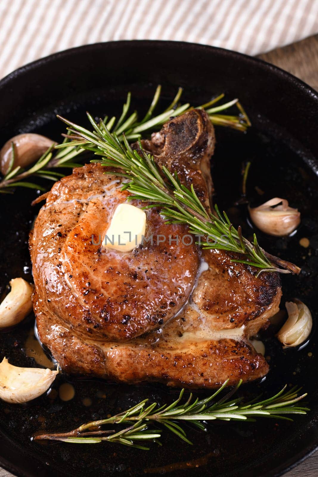 Pork cutlet on the bone in a piece of butter with garlic and rosemary in a frying pan 