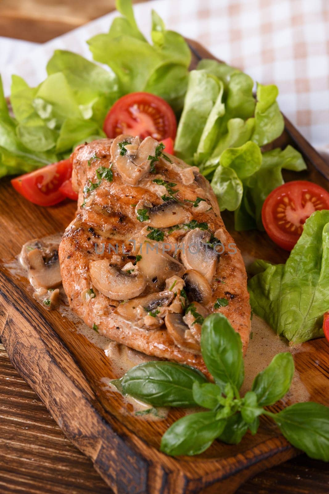 Chicken breast with mushroom sauce and vegetables on a wooden plate