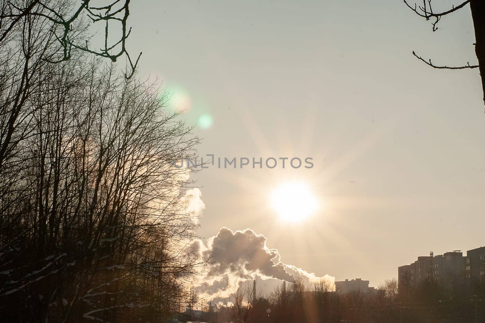 Cityscape with a smoking chimney from a heating station, sky, snow, sun.