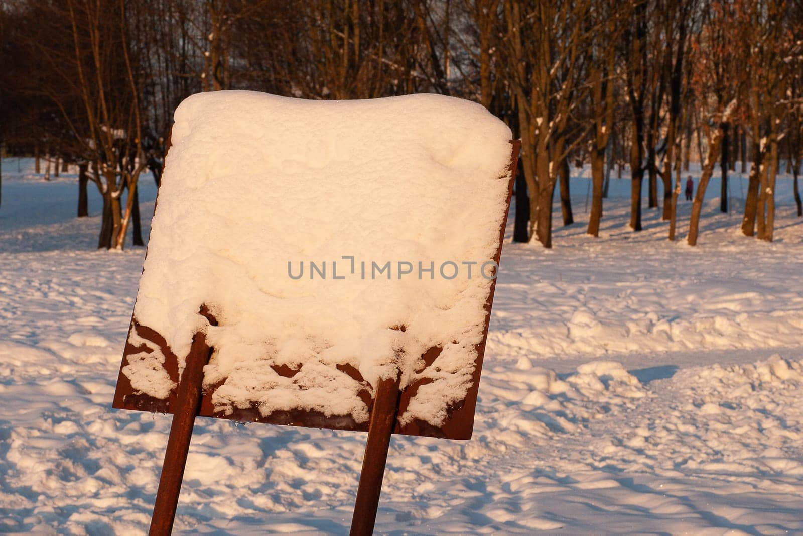 A wooden, snow-covered, leaning information sign in the forest.