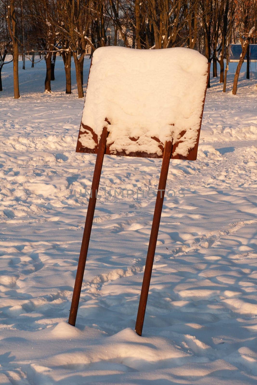 A wooden, snow-covered, leaning information sign in the forest.