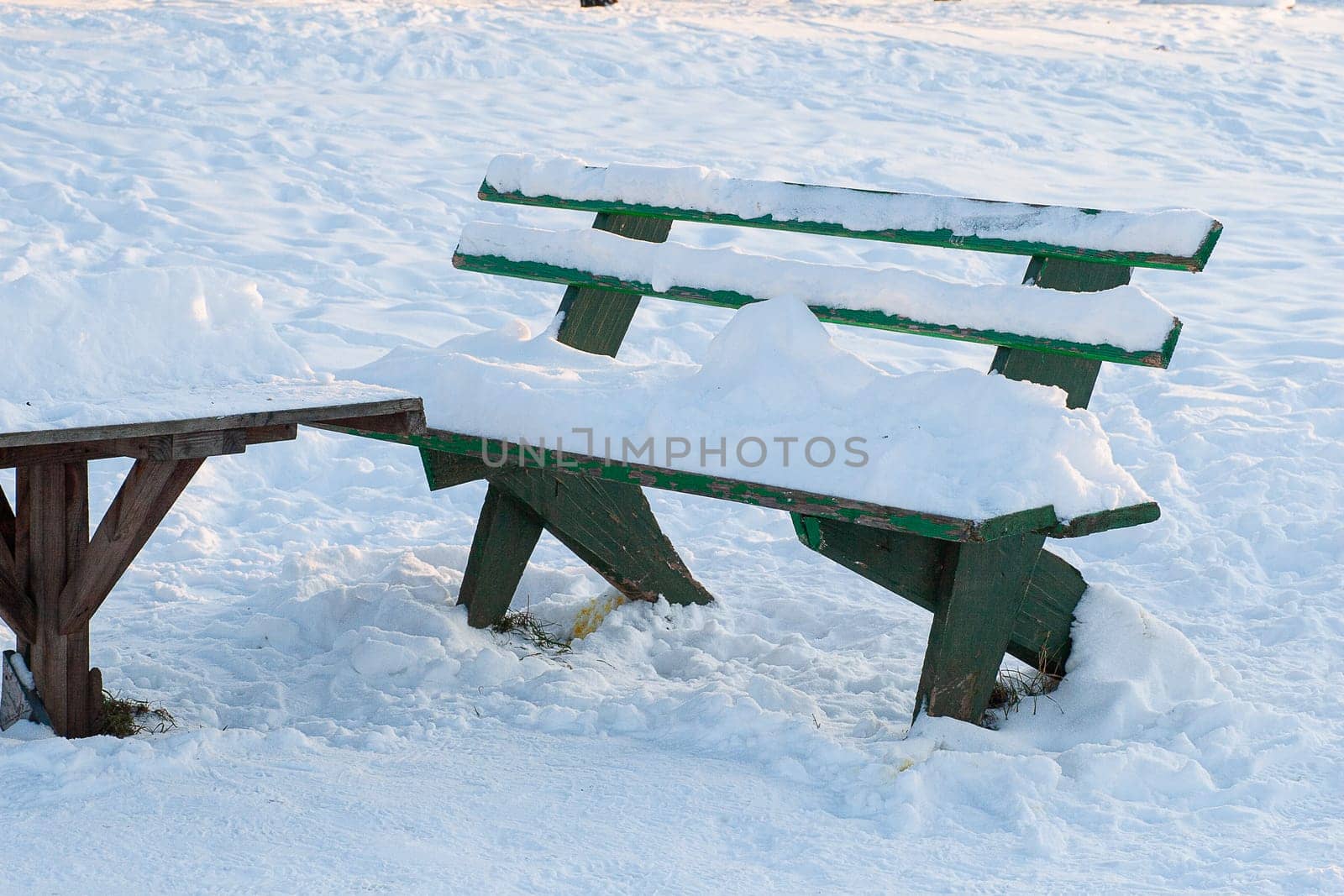 Wooden green bench and table covered with snow against the background of a snowy surface.