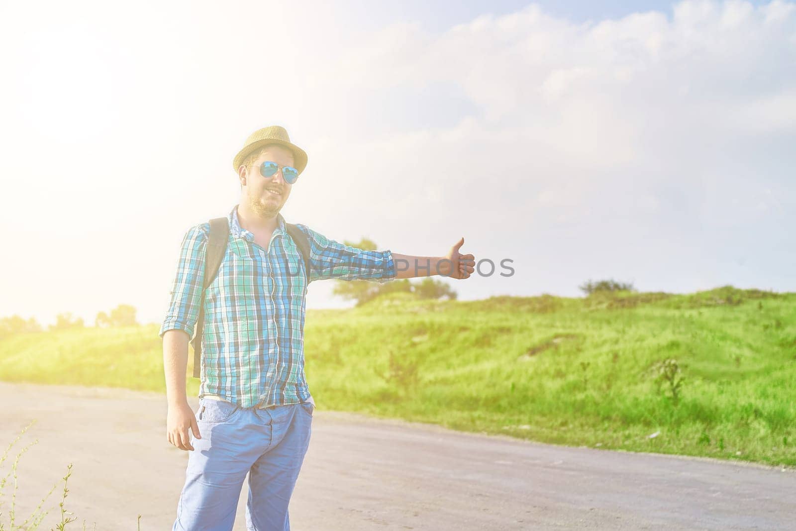 Hitchhiker with backpack in summer hat, light shirt, shorts on the road in tropical country in Sunny weather at summer