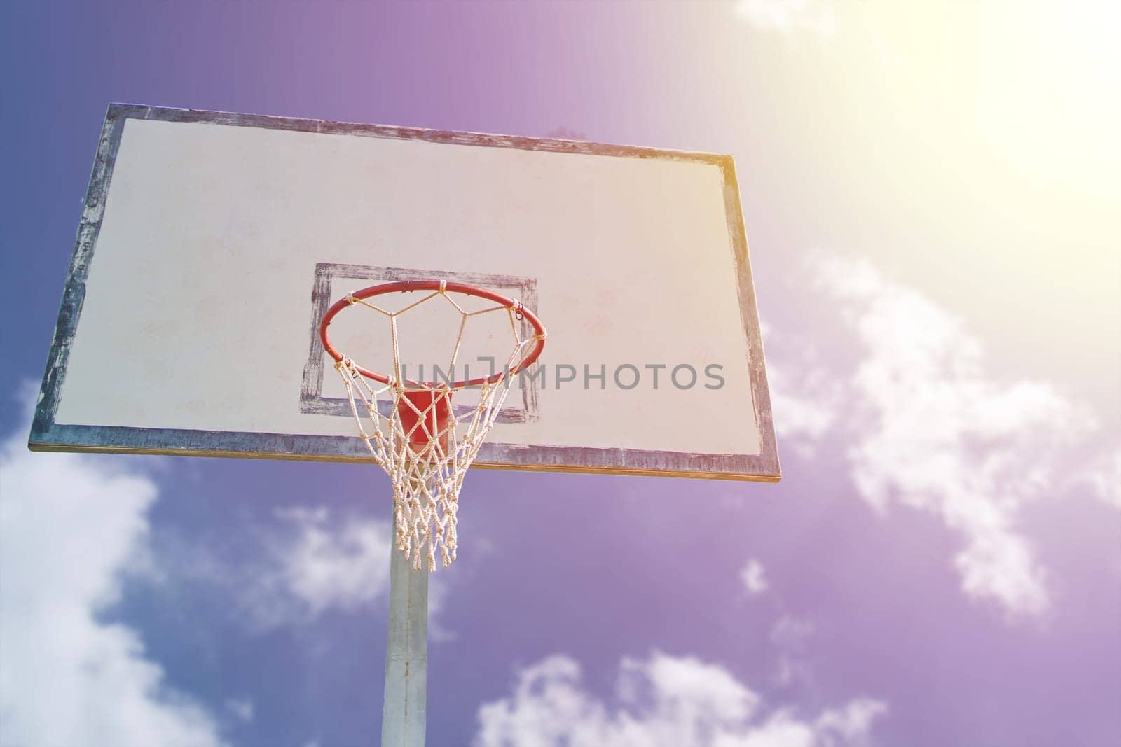 Orange basketball rim with white net and wooden backboard against blue sky