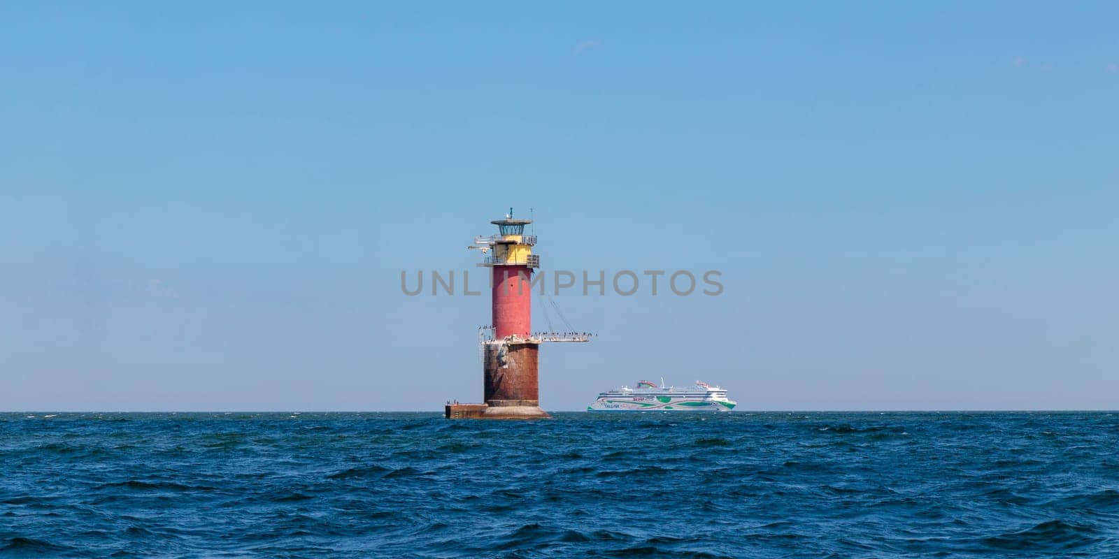 Gulf of Finland, Estonia, June 28, 2024 -A lighthouse in the Baltic Sea near Tallinn and ferry Tallink from Helsinki. Blue sky, clouds, waves, sea. Banner with copy space
