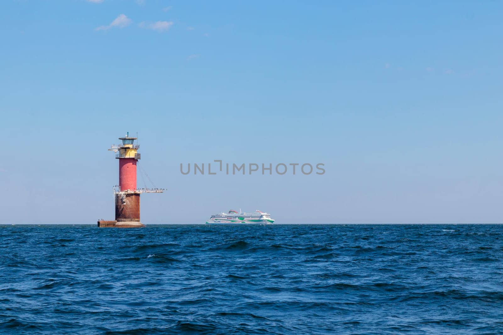 Gulf of Finland, Estonia, June 28, 2024 -A lighthouse in the Baltic Sea near Tallinn and ferry Tallink from Helsinki. Blue sky, clouds, waves, sea. Banner with copy space